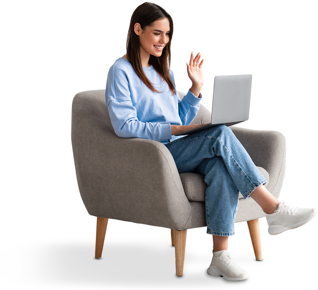 Eine Frau sitzt im Sessel, lächelt und winkt in den Laptop auf ihrem Schoß